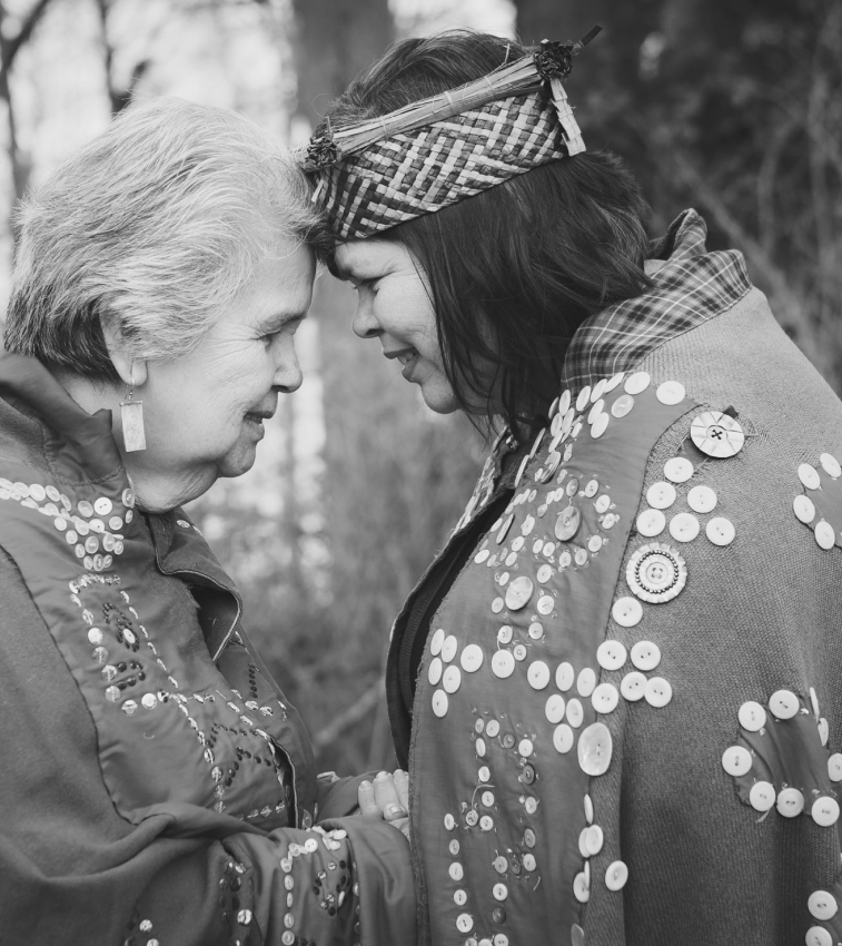 Greyscale photo of an elder and a woman facing each other with their foreheads touching
